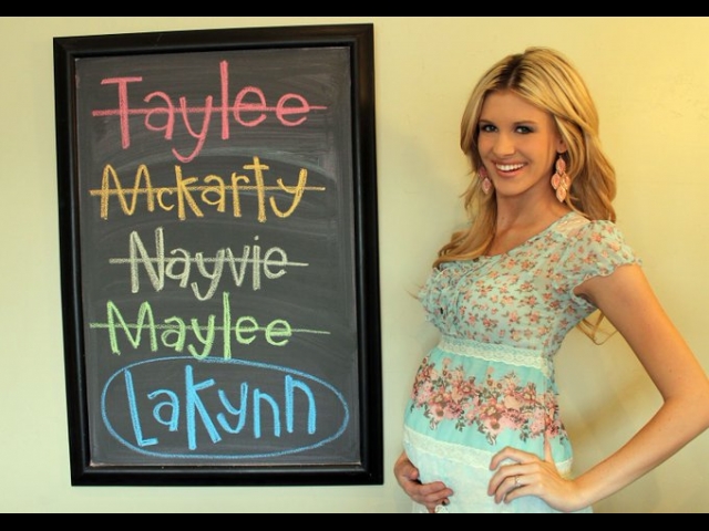 A blonde posing with a hand under her pregnancy bump, next to a chalkboard with a list of potential baby names crossed out: Taylee, McKarty, Nayvie, Maylee... and then at the bottom, a circled name that she apparently had settled on for the baby: Lakynn.